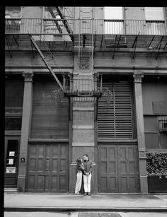 black and white photograph of two people standing in front of a building with fire escapes