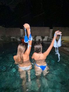 two women in blue bikinis are standing in the water with their arms raised up