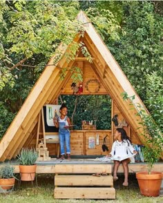 two children are standing on the roof of a small house made out of wooden planks