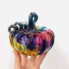 a hand holding a colorful glass pumpkin in front of a white background with the bottom painted multicolored