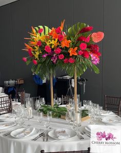 an arrangement of flowers on a table with wine glasses and place settings in front of it