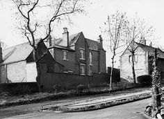 an old black and white photo of people sitting on the curb in front of houses