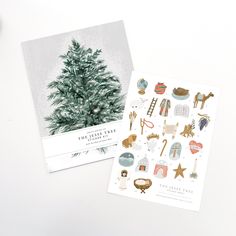 two christmas cards sitting next to each other on top of a white table with decorations