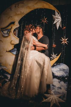 a bride and groom kissing in front of a moon with stars hanging from the ceiling