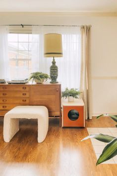 a living room filled with furniture and a lamp on top of a wooden dresser next to a window