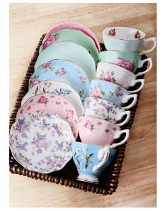 a basket filled with lots of different colored cups and saucers on top of a wooden table