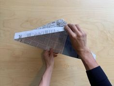 two hands are holding an origami airplane on a wooden surface with paper attached to it