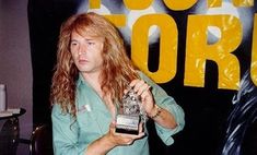 a man with long hair holding an award in front of a poster that reads foo stork