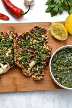 grilled chicken with green sauce on a cutting board next to lemons and parsley