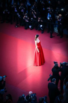 a woman in a red dress is standing on a red carpet with cameras around her