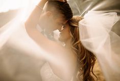 a bride and groom posing for a photo with veil blowing in the wind behind them