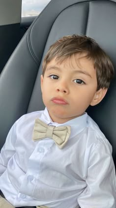 a young boy wearing a white shirt and bow tie sitting in the back seat of a car