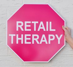 a pink stop sign with the words retail therapy written on it, in front of a white brick wall