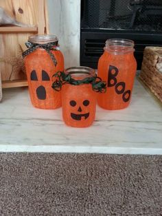 three mason jars decorated like pumpkins with faces painted on them sitting on a mantle