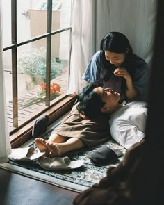 two people laying on the floor in front of a window