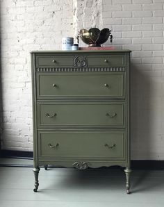 a green chest of drawers in front of a brick wall with an iron pot on top