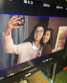 a woman taking a selfie with her friend on the tv screen in front of her