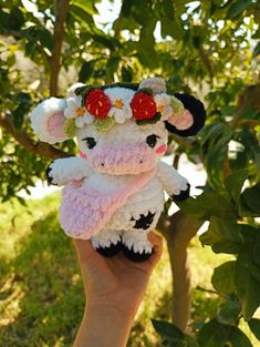 a hand holding a small stuffed animal with flowers on it's head and ears