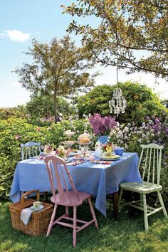 a table with blue cloths and pink chairs in the middle of a field full of flowers