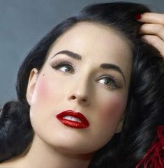 a woman with dark hair and red lipstick is posing for the camera, she has her hand on her head