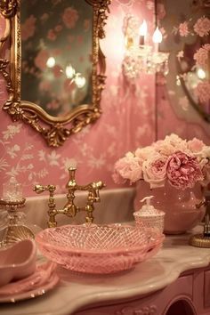 a pink bathroom with gold accents and flowers on the counter top, along with an ornately decorated mirror