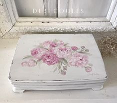 an old white box with pink flowers painted on it sitting in front of a window