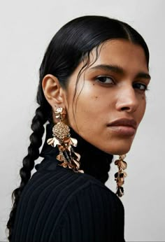 a woman with braids and earrings on her head looking off to the side,