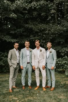 a group of men standing next to each other in front of some trees and grass