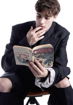 a man in a suit sitting down reading a book with his hand on his chin