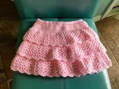 a pink crocheted skirt sitting on top of a green chair next to a pillow