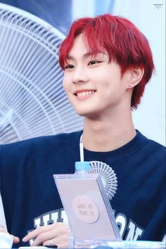 a young man with red hair is smiling and holding an object in his hand while sitting at a table