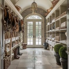 a large walk in closet with lots of shoes on the shelves next to doors and potted plants