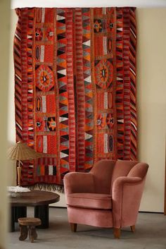 an orange chair sitting in front of a colorful wall hanging