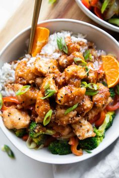 a bowl filled with chicken and vegetables on top of rice next to an orange slice