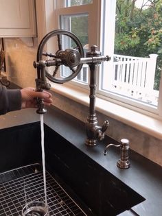 a person washing their hands under a faucet in a kitchen sink next to a window