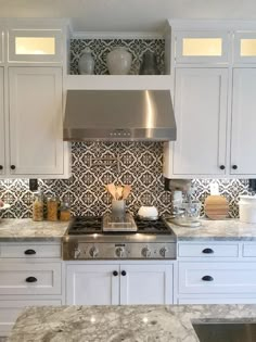 a kitchen with white cabinets and marble counter tops, stainless steel range hood over the stove