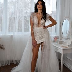 a woman standing in front of a window wearing a white dress with feathers on it