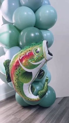 a fish balloon sitting on top of a wooden floor next to green and white balloons