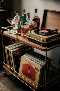 a record player sitting on top of a metal cart filled with vinyl records and liquor bottles