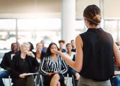 a woman standing in front of a group of people with her hand out to the side