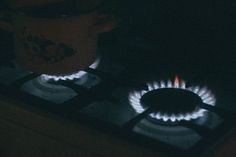 a gas stove with two burners lit up in the dark, next to a coffee mug