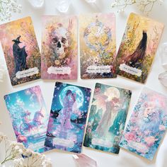 five cards with different designs on them sitting next to white flowers and crystals in the background