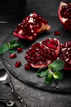 pomegranates with leaves and mint on a slate board next to a spoon