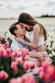 a man and woman are sitting in the middle of flowers with their arms around each other