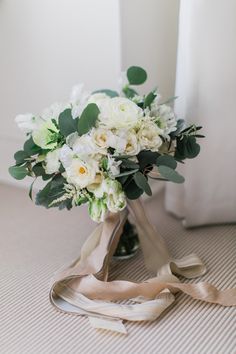 a bridal bouquet with white flowers and greenery sits on the floor in front of a window