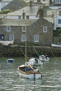 several small sailboats in the water near some buildings and stone wall with windows on each side