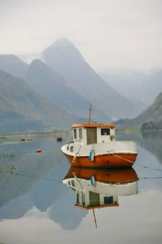 an orange and white boat sitting on top of a body of water next to mountains