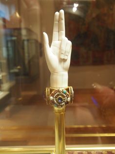 a hand that is sitting on top of a gold stand in front of a glass window