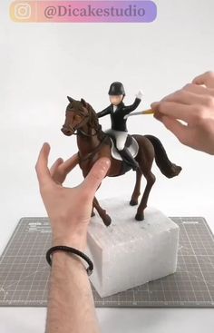 a hand is holding a toy horse and pointing it at the figurine