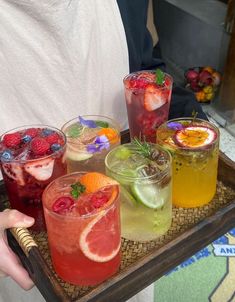 there are many drinks on the tray and one is holding a strawberries, oranges, raspberry